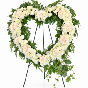 Forever in Our Hearts heart-shaped funeral wreath featuring ivory roses, white chrysanthemums, and cascading greenery displayed on a standing easel by Sassafraz Flowers, Galena, Ohio.