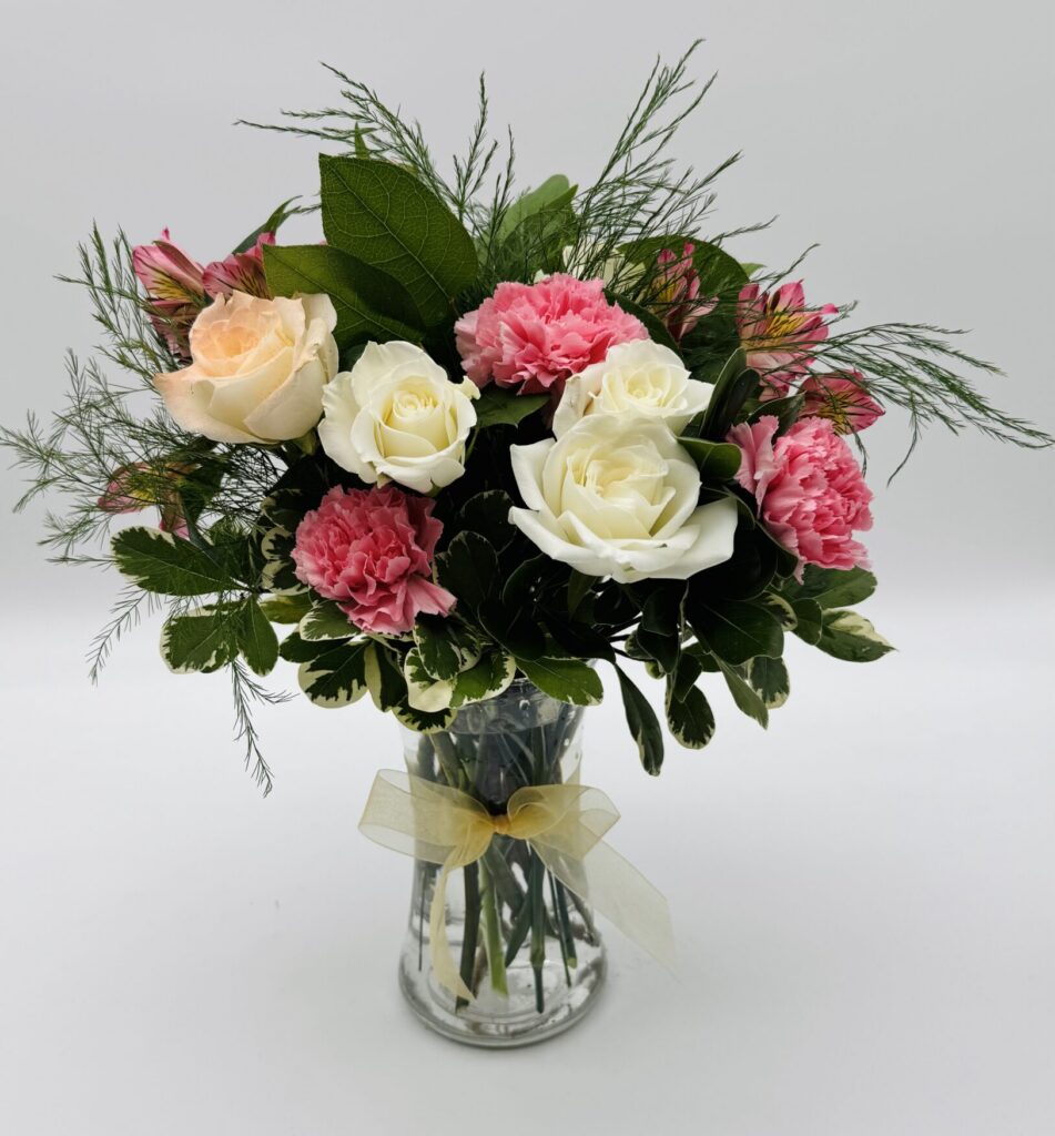 Pink Silk floral arrangement featuring ivory and blush roses, pink carnations, pink alstroemeria, and lush greenery in a clear glass vase with a gold ribbon by Sassafraz Flowers, Galena, Ohio.