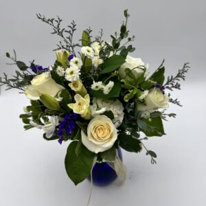 Reflections floral arrangement featuring ivory roses, white seasonal blooms, deep blue accents, and greenery in a cobalt blue vase by Sassafraz Flowers, Galena, Ohio.